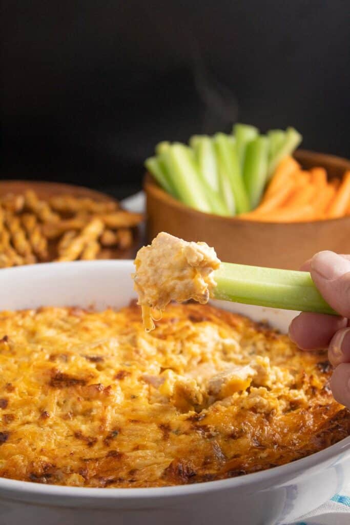 A celery stick dipped into a cheesy dip with steam coming off of it.