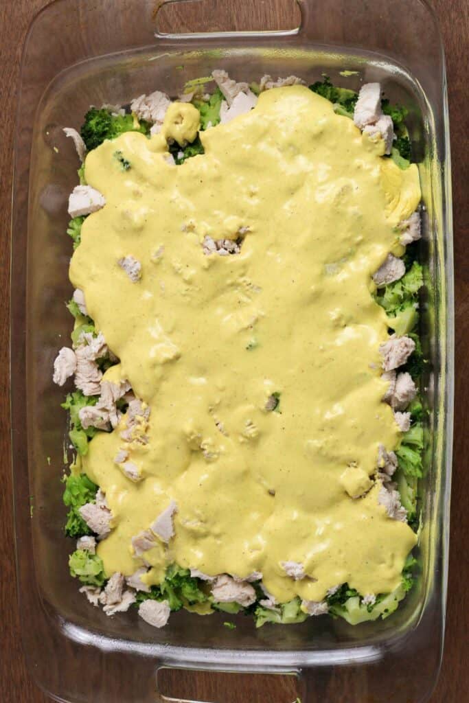 A layer of curry sauce covering the broccoli and chicken in a casserole dish.