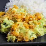 A vibrant yellow casserole with broccoli, chicken, and cheese next to a pile of white rice on a black plate.