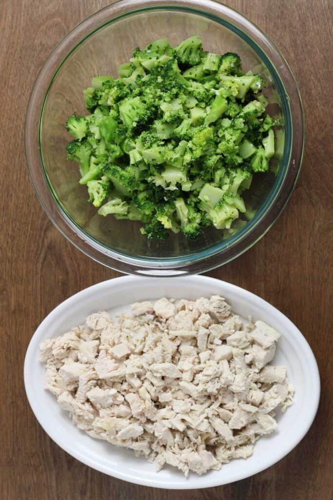 Prepared steamed broccoli and cubed chicken in bowls on a wooden surface.