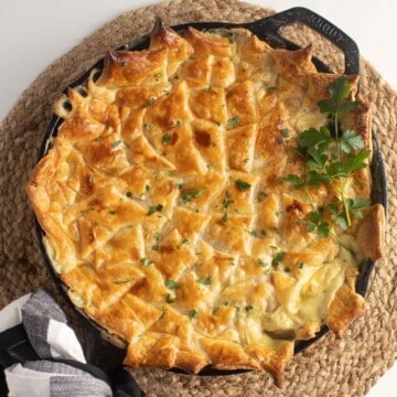 A cast iron skillet pot pie with a golden pastry crust sitting atop a brown woven background.