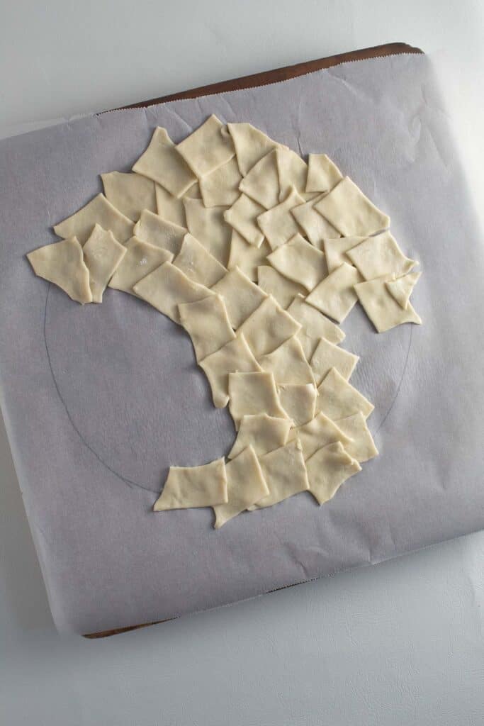 Small pieces of puff pastry being arranged into a circle on a piece of parchment paper.