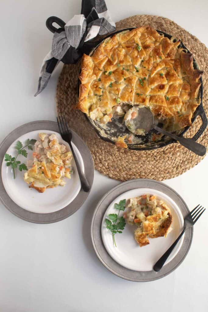 Two servings of Creamy Chicken or Turkey Pot Pie with Puff Pastry Crust are on white plates with the remaining pie in a cast iron skillet.