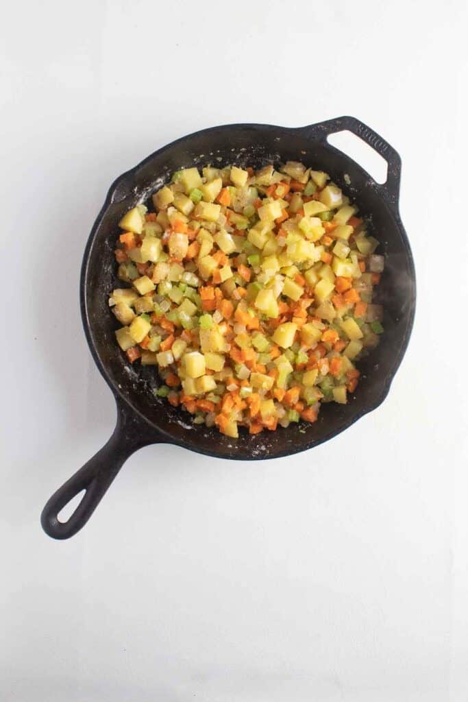 Vegetables cooking in a cast iron skillet with steam rising above.