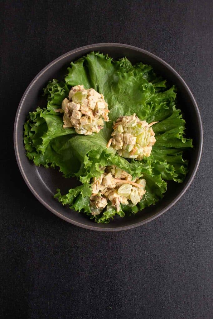 Curry chicken salad with grapes served on a bed of lettuce on a black background.