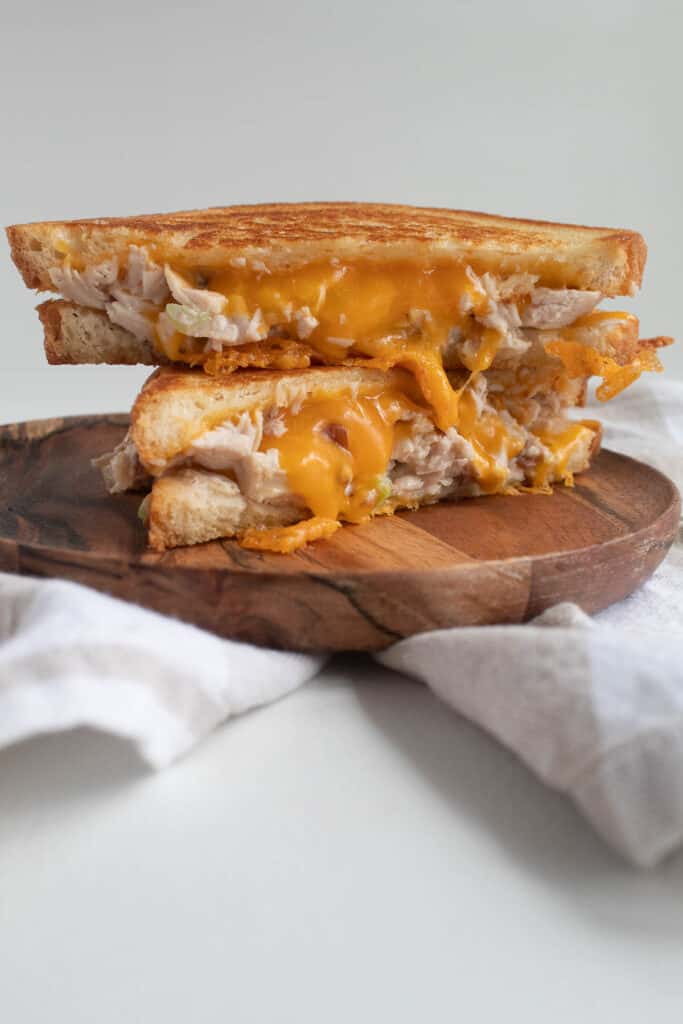 Two halves of a chicken pecan salad melt stacked in a tower on a wooden plate with orange cheddar melting out of the center.