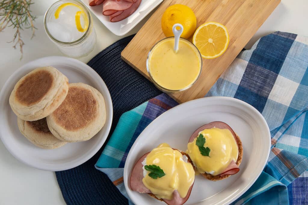 English muffins, ham, and microwave hollandaise arranged around a plate of eggs Benedict with parsley garnish.