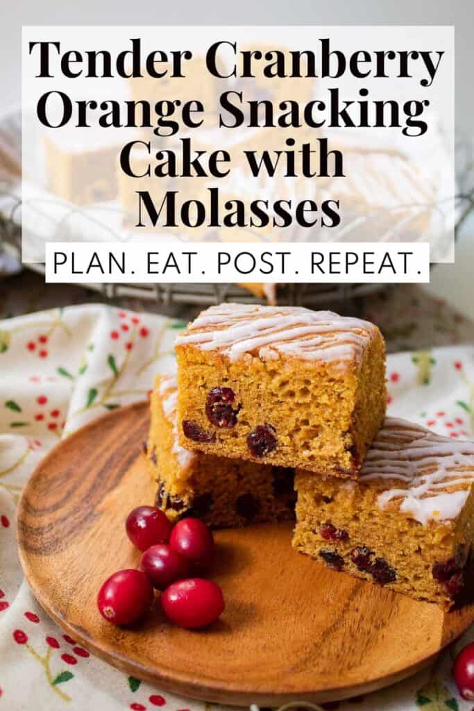 A wooden plate holding three squares of a golden cake studded with cranberries and drizzled with a white glaze. The words, "Tender Cranberry Orange Snacking Cake with Molasses" and "Plan. Eat. Post. Repeat." in a box at the top of the image.