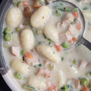 A bowl of creamy white soup with gnocchi, chicken, peas, carrots, and green beans visible.