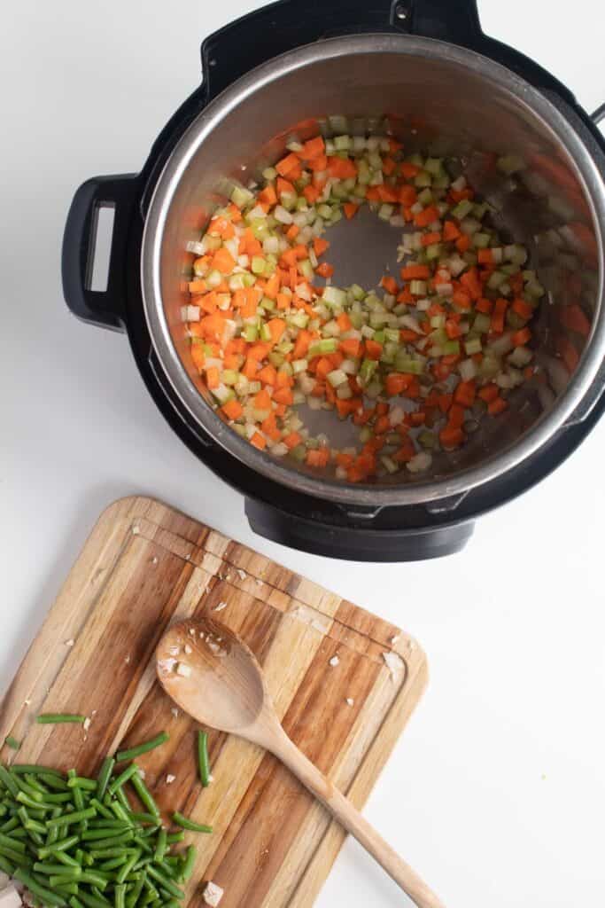 Vegetables cooking in the bowl of an Instant Pot next to a cutting board with cut green beans on it.