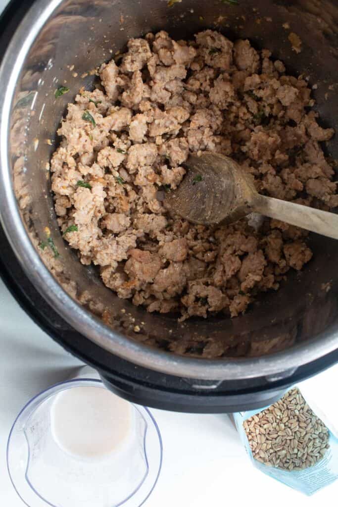 Cooked sausage and oregano leaves in the insert of an instant pot.