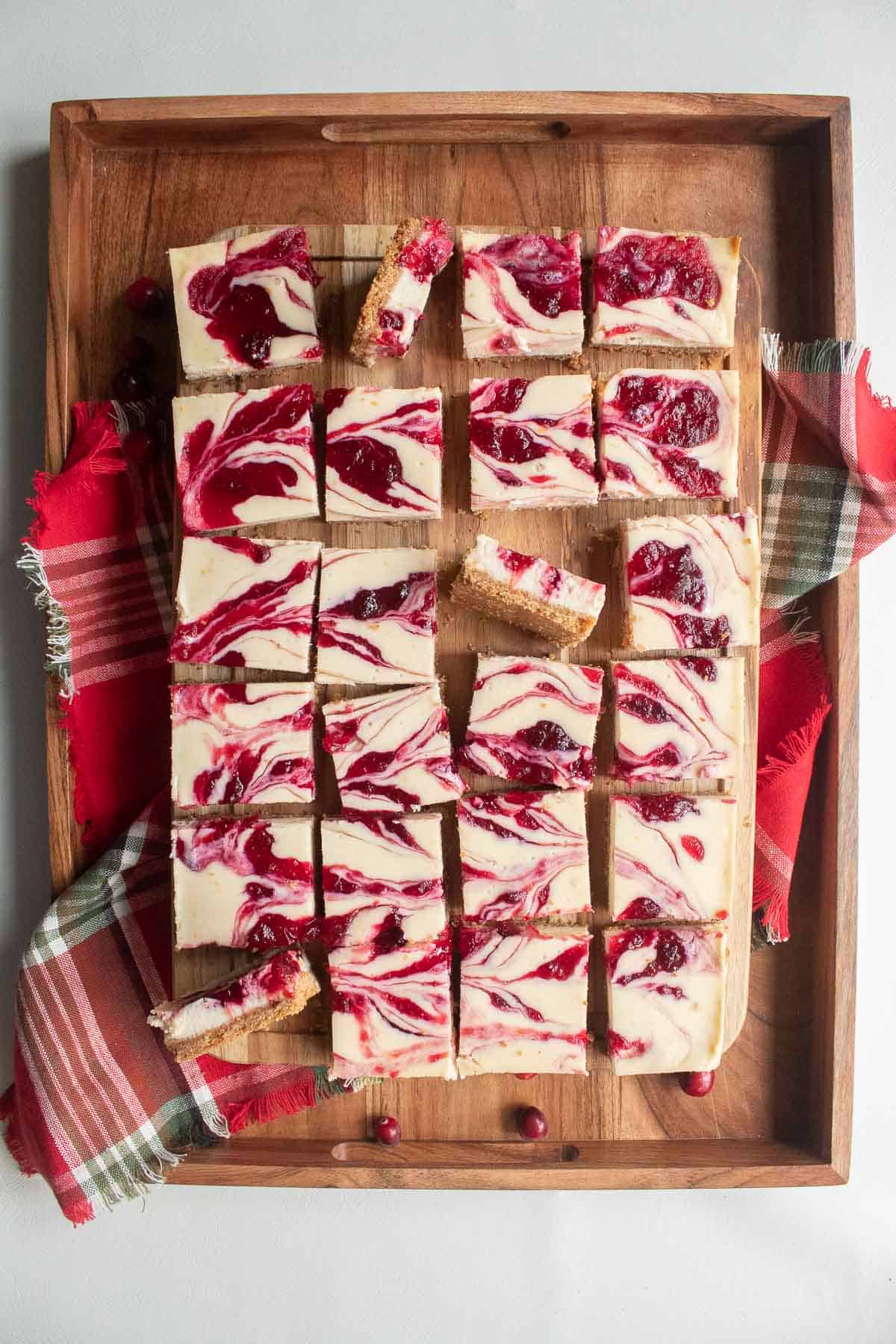 Marbled red and white cheesecake bars arranged on a wooden cutting board over a red and green plaid cloth.