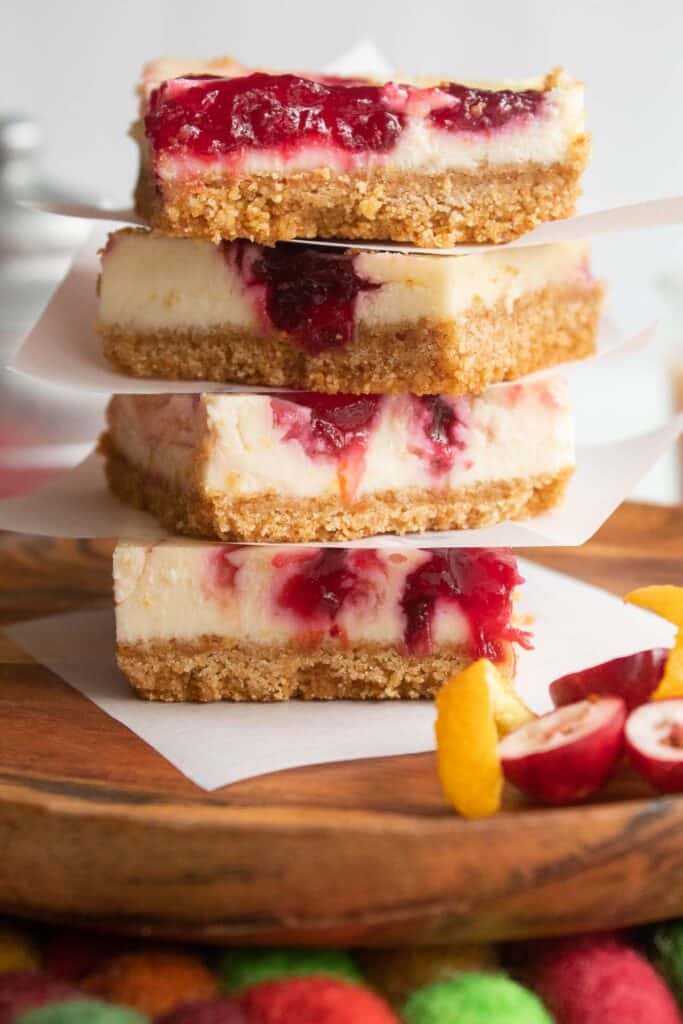 A stack of red and white dessert bars with brown graham cracker crust sitting on a wood plate.
