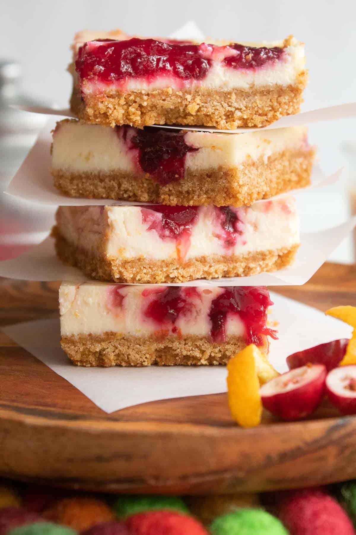 A stack of red and white dessert bars with brown graham cracker crust sitting on a wood plate.