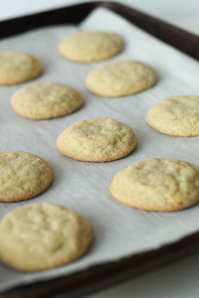 A dozen baked cookies on a baking tray, with golden edges and sugared tops.