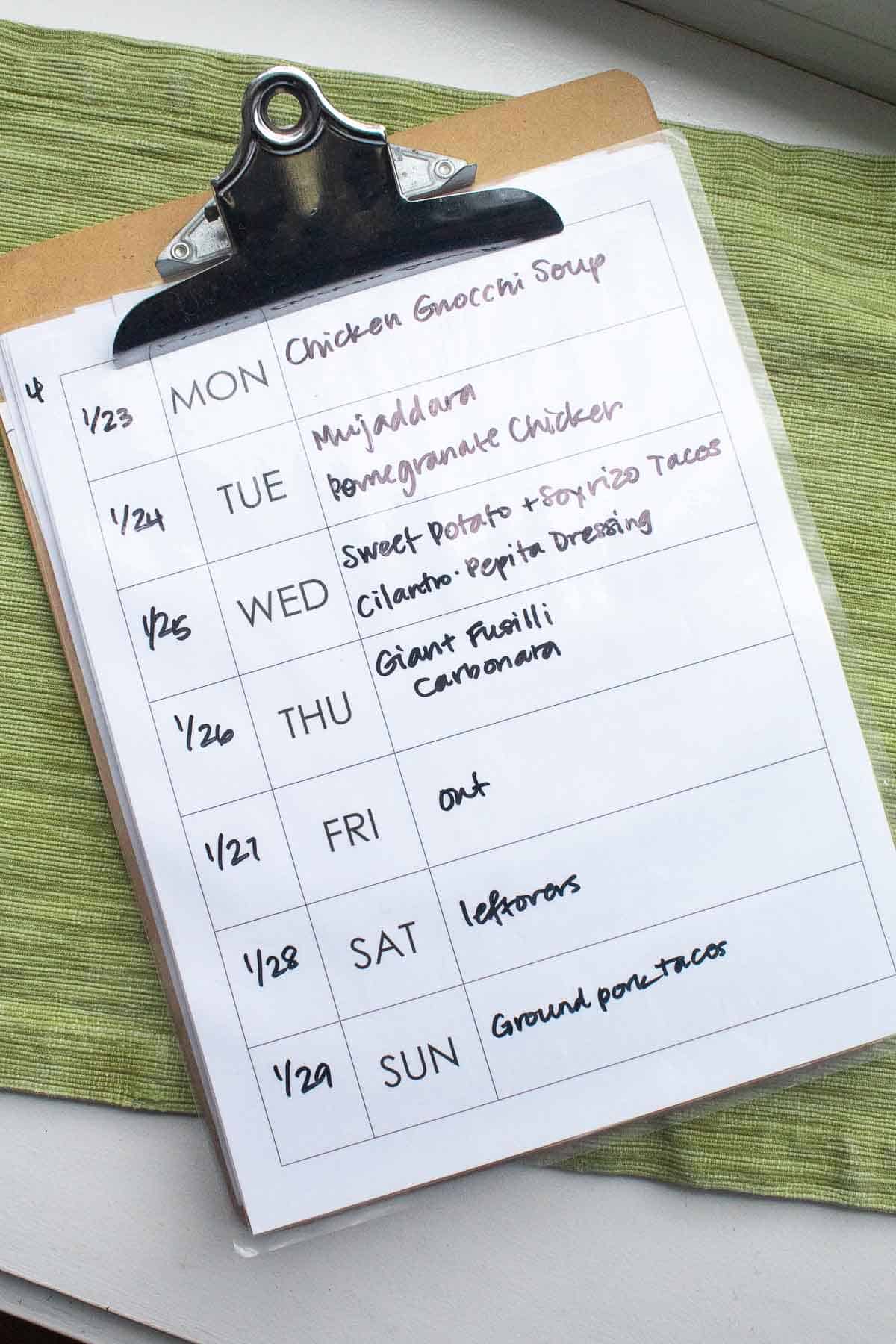 The weekly meal plan written out on a laminated sheet attached to a clip board.