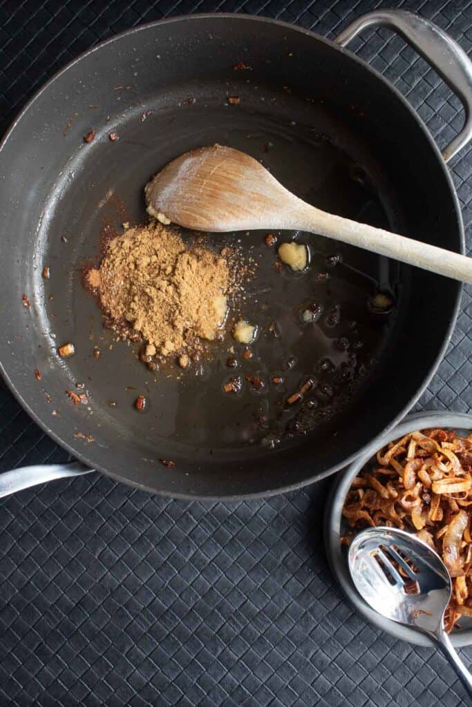 The spices being added to the oil remaining in the skillet after the shallots are removed.