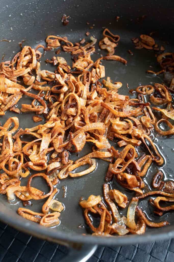 Shallots crisping up in oil in a deep skillet.