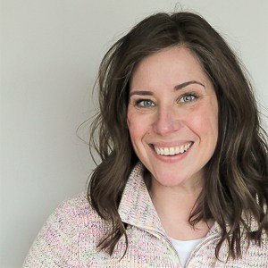 Cassie wearing a collared sweater in front of a gray wall.