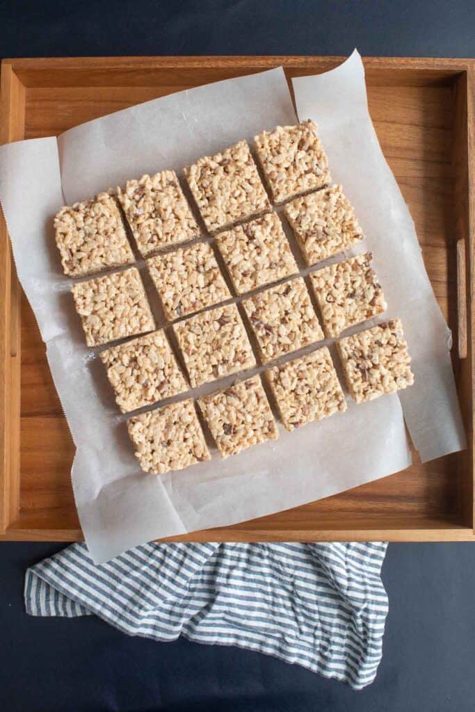 The batch of rice krispie treats cut into 16 squares and placed on a wooden platter.
