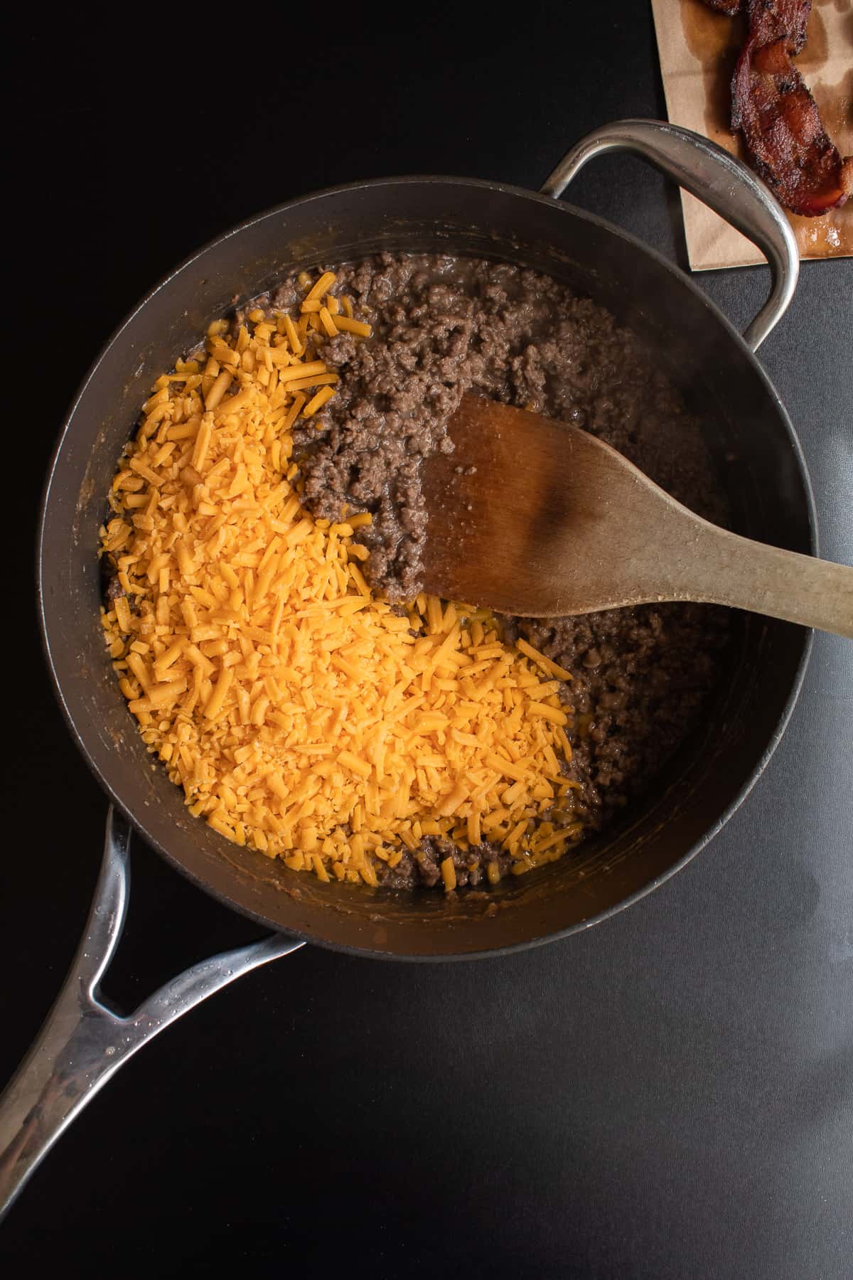 Cheddar cheese being stirred into the seasoned ground beef in a skillet.