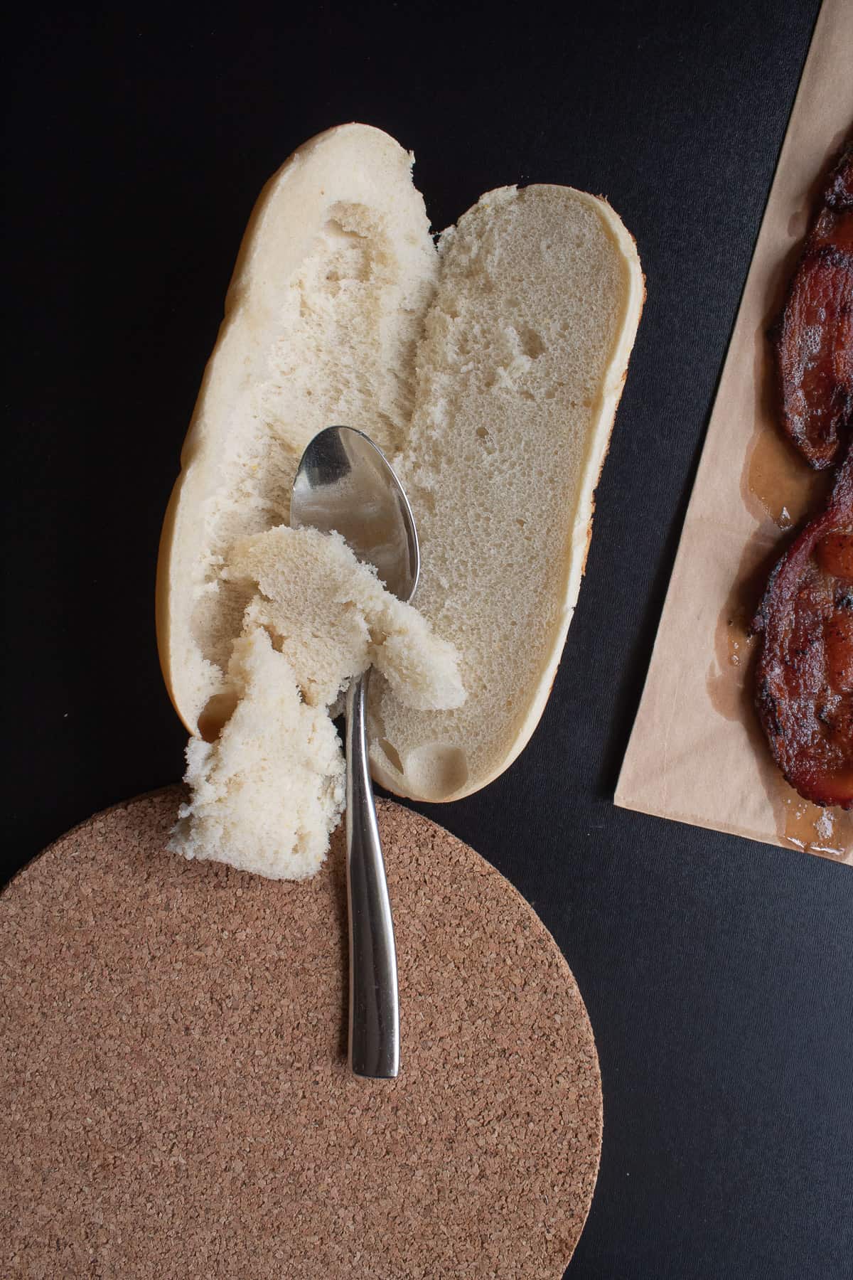 Scooping the excess bread out of a roll with a spoon to make more room for filling.