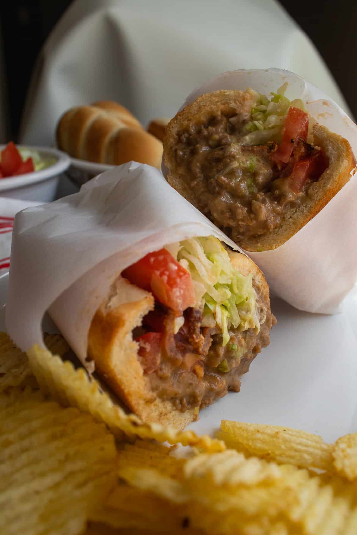 A cheeseburger sub wrapped in white parchment paper and sliced in half to show the texture and toppings.