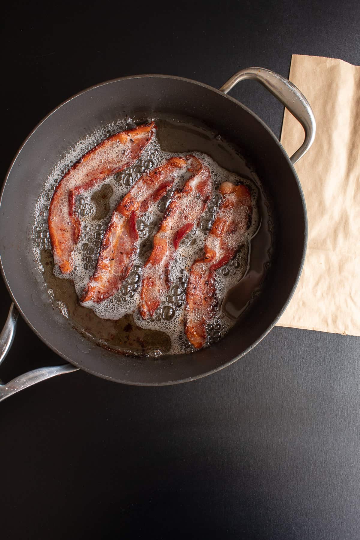 Four slices of baking frying in a skillet.