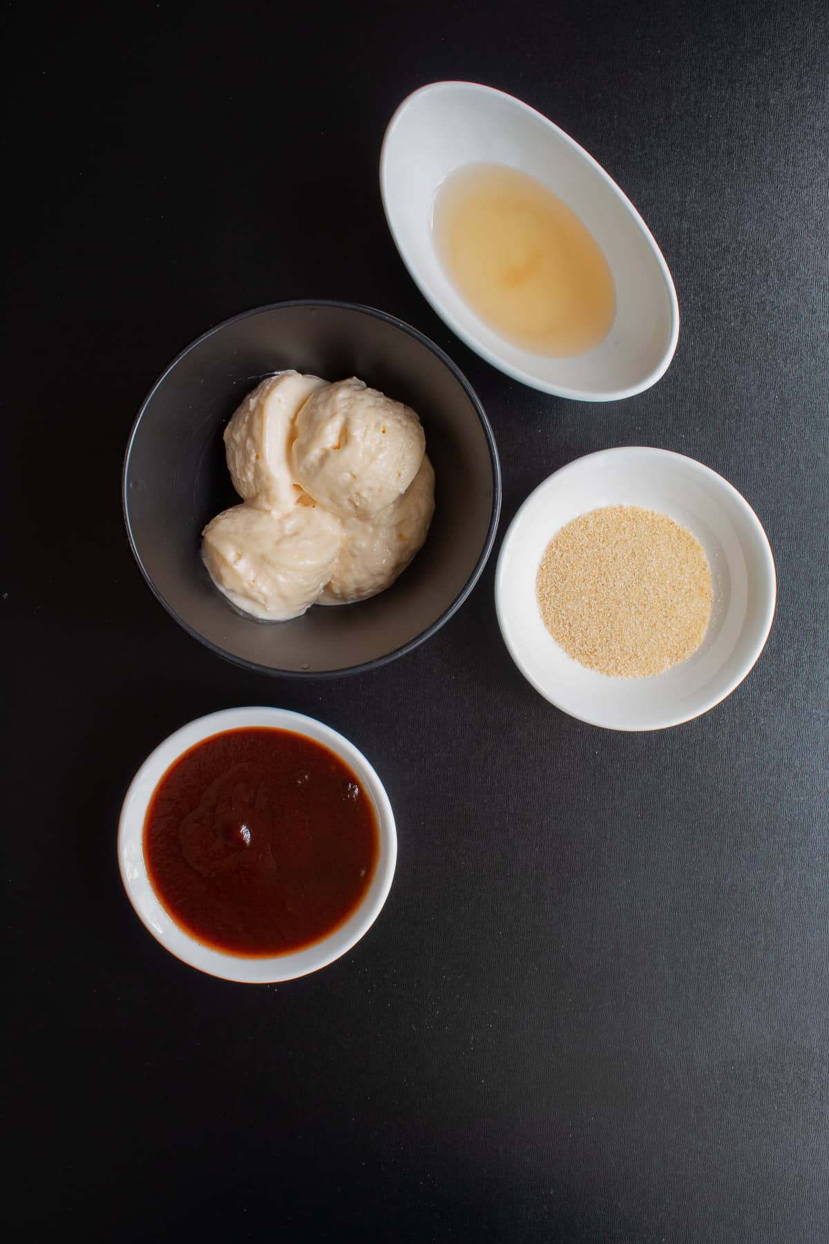 Ingredients for the special sauce arranged in small bowls on a black surface.