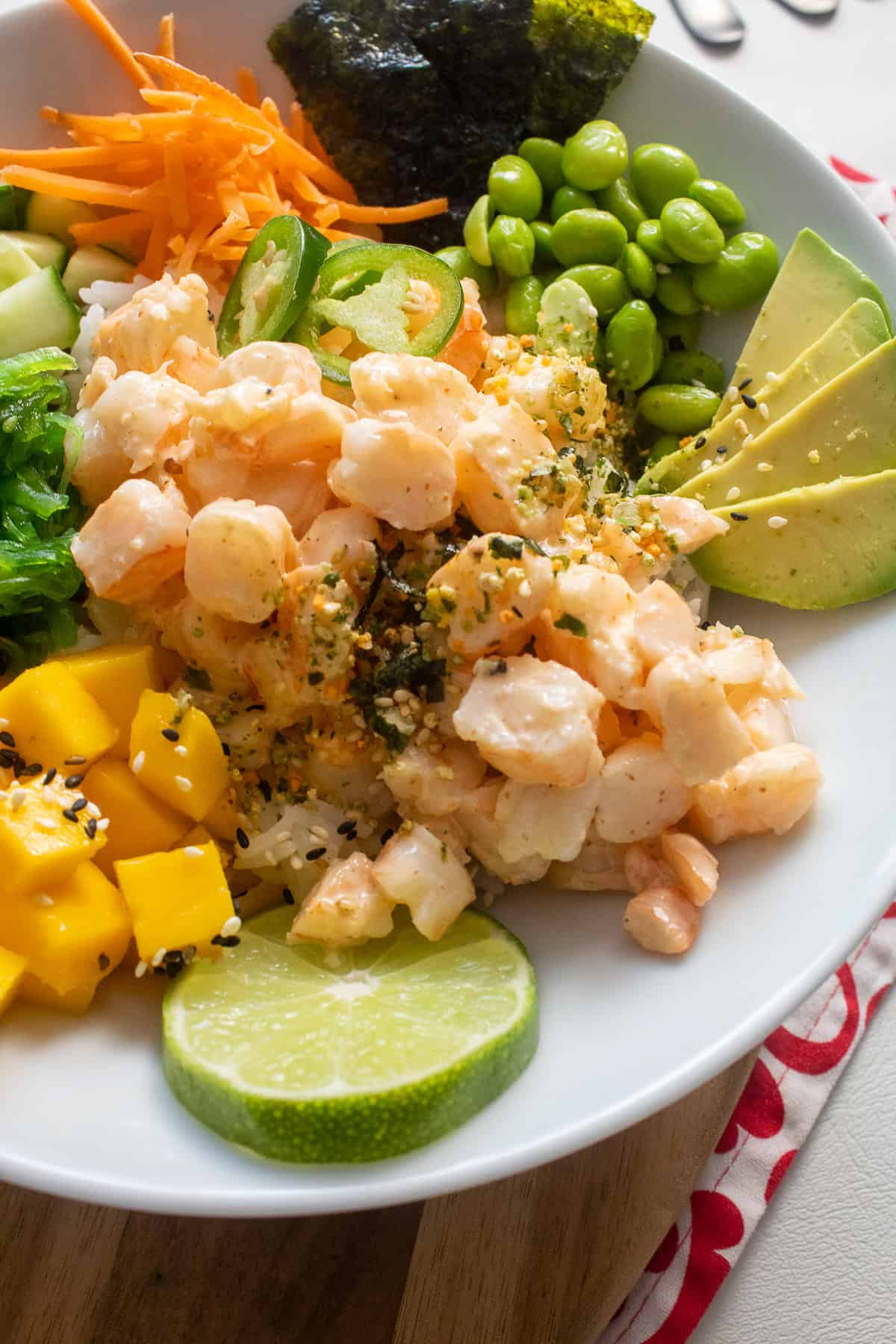Detail of a white bowl containing shrimp poke and a variety of toppings.