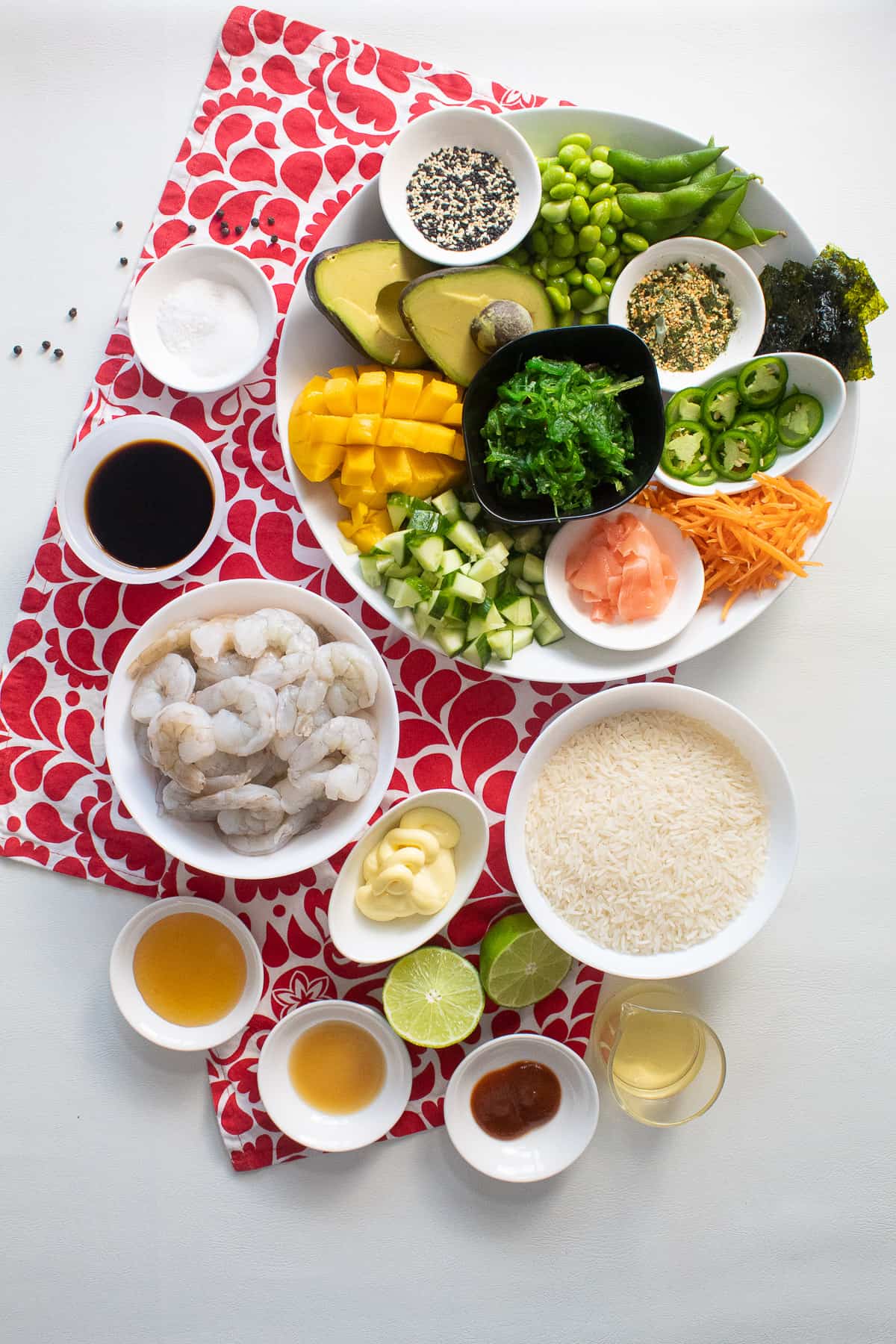 The ingredients for the poke bowls are arranged on a white surface and a red and white patterned cloth.