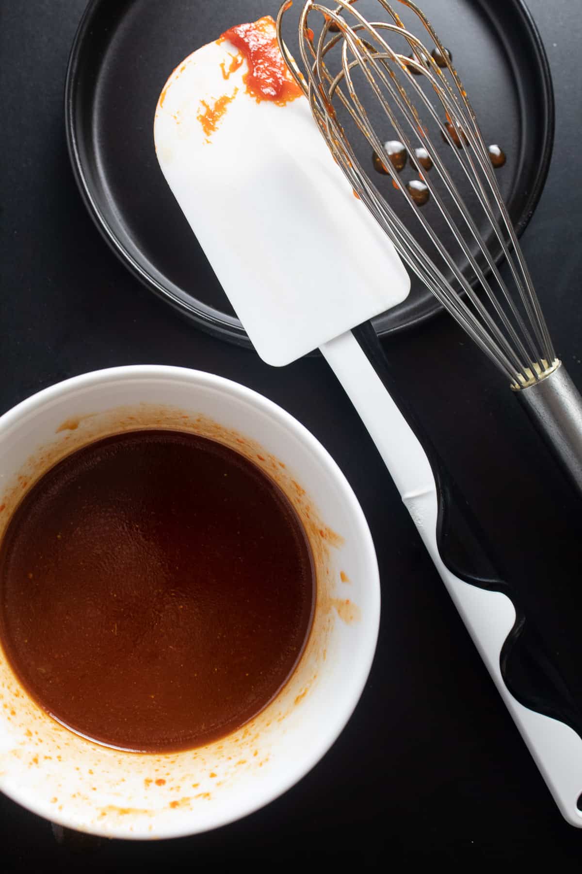 The rich red sauce is in a white bowl on a black surface with utensils nearby.