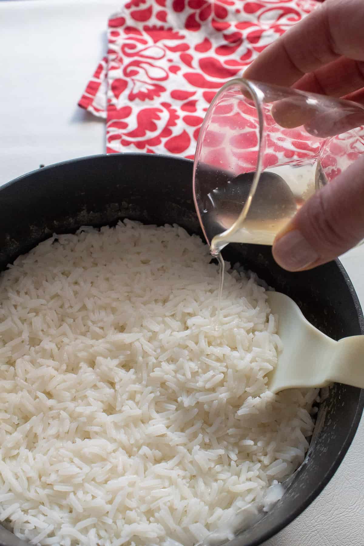 Cooked rice in a saucepan is being seasoned with a mixture of vinegar, salt, and sugar.