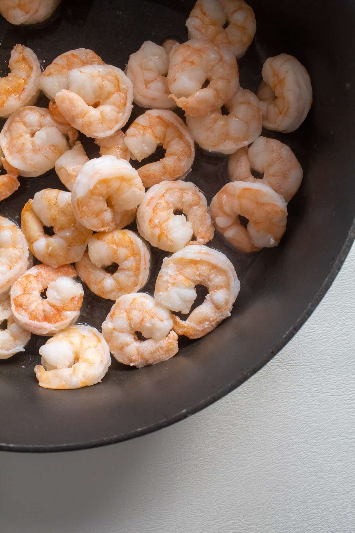 Whole cooked shrimp sit in the bottom of a dark frying pan.