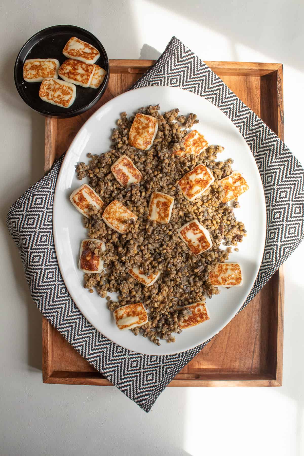 Halloumi cheese is nestled into the layer of lentils on a white platter.