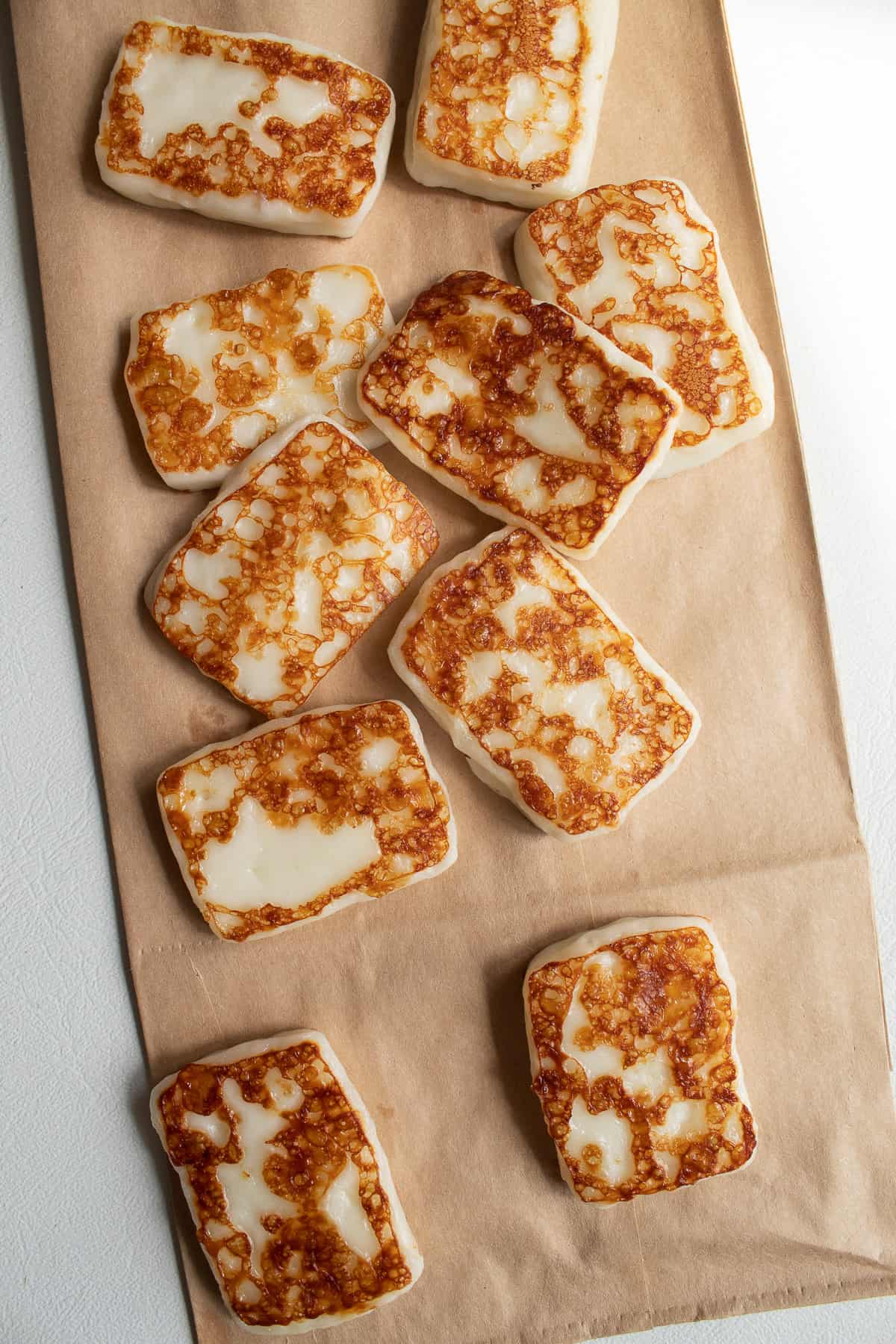 Fried halloumi pieces draining on a brown paper bag.