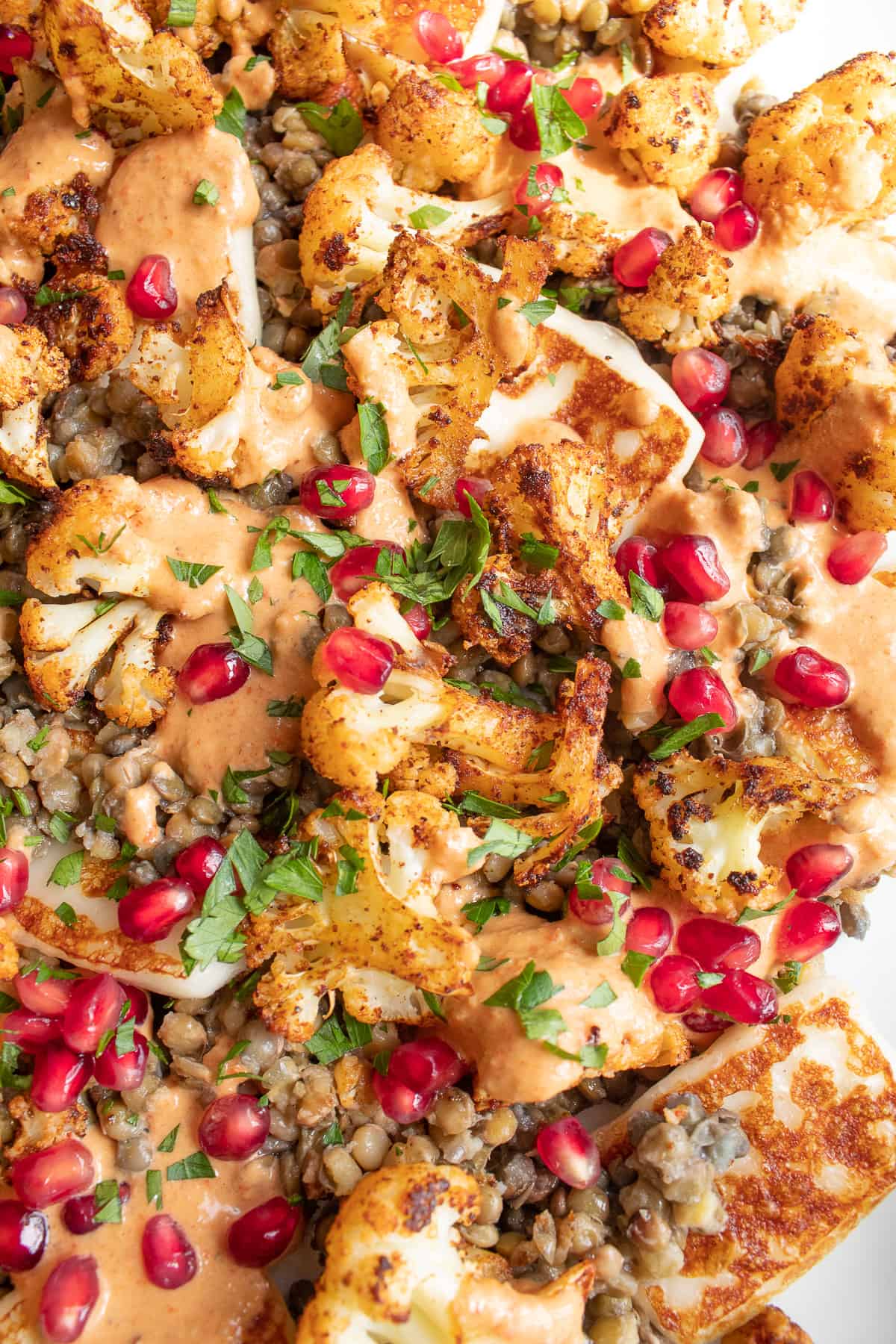 A detailed image of the salad with lentils, fried halloumi, roasted cauliflower, chopped parsley, an orange dressing, and red pomegranate arils.