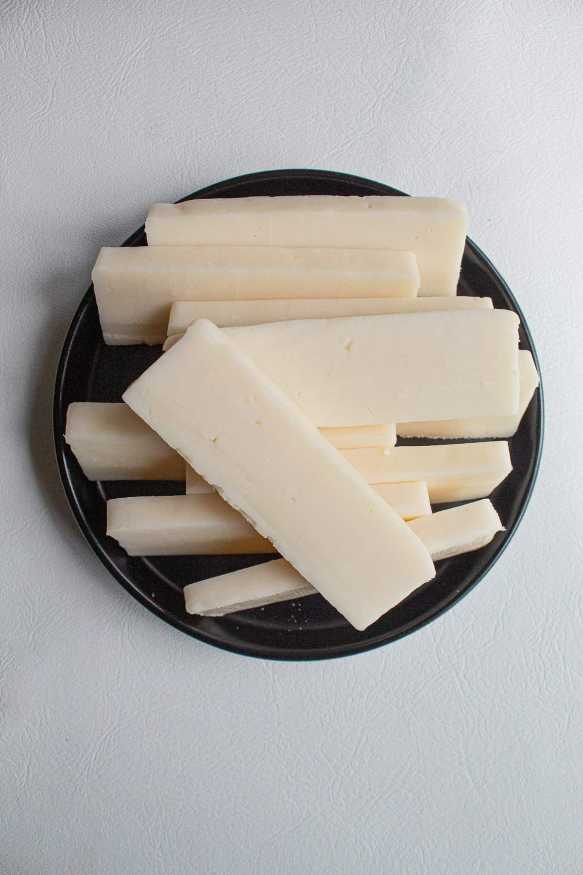 Slices of fresh halloumi cheese are piled on to a black plate.