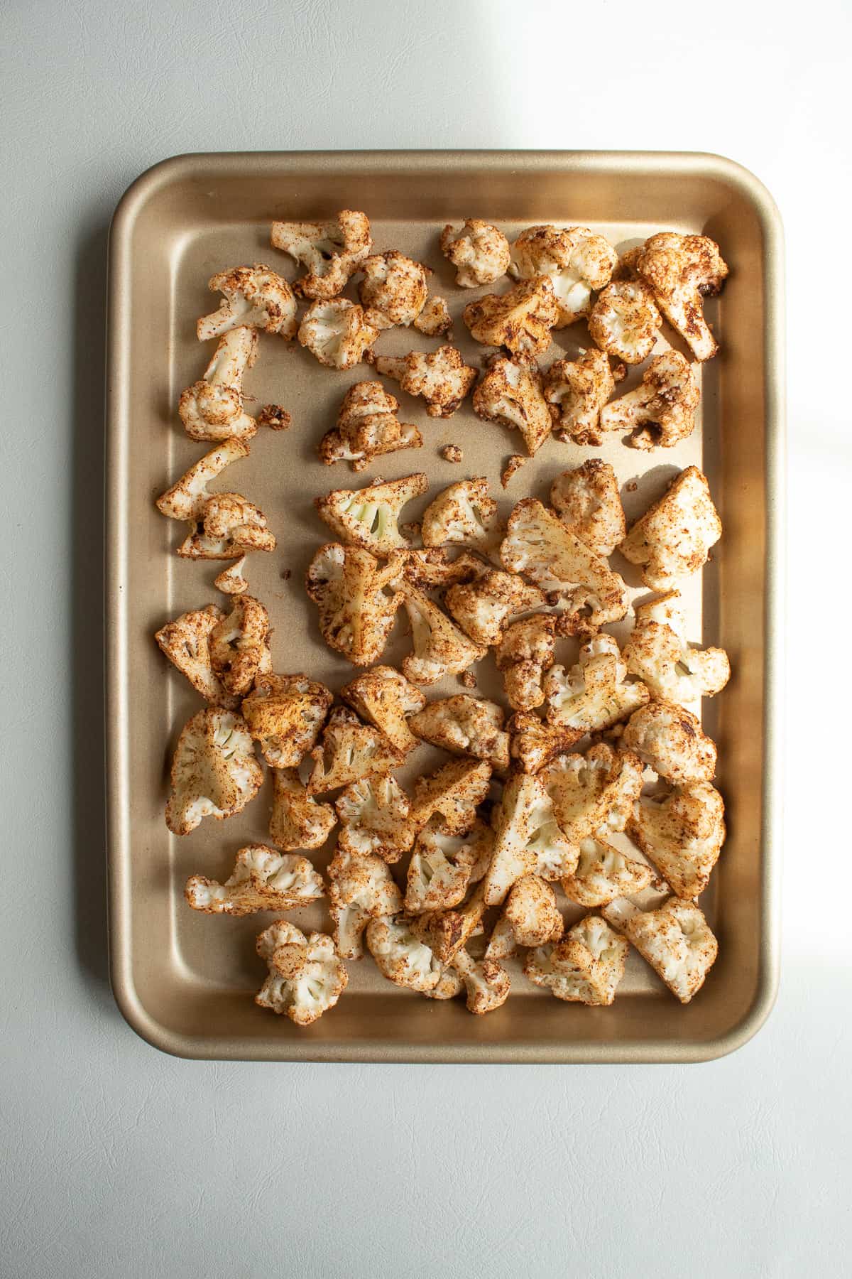 The seasoned cauliflower florets spread out over a small sheet pan.
