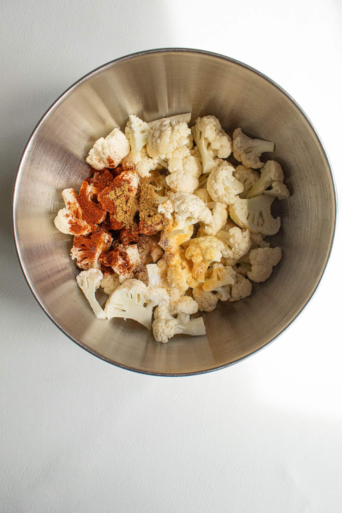 Cauliflower florets in a stainless steel bowl with spices sprinkled over the top.