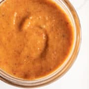 A reddish-orange dressing with specks of black pepper and roasted red pepper is swirled in a glass jar.