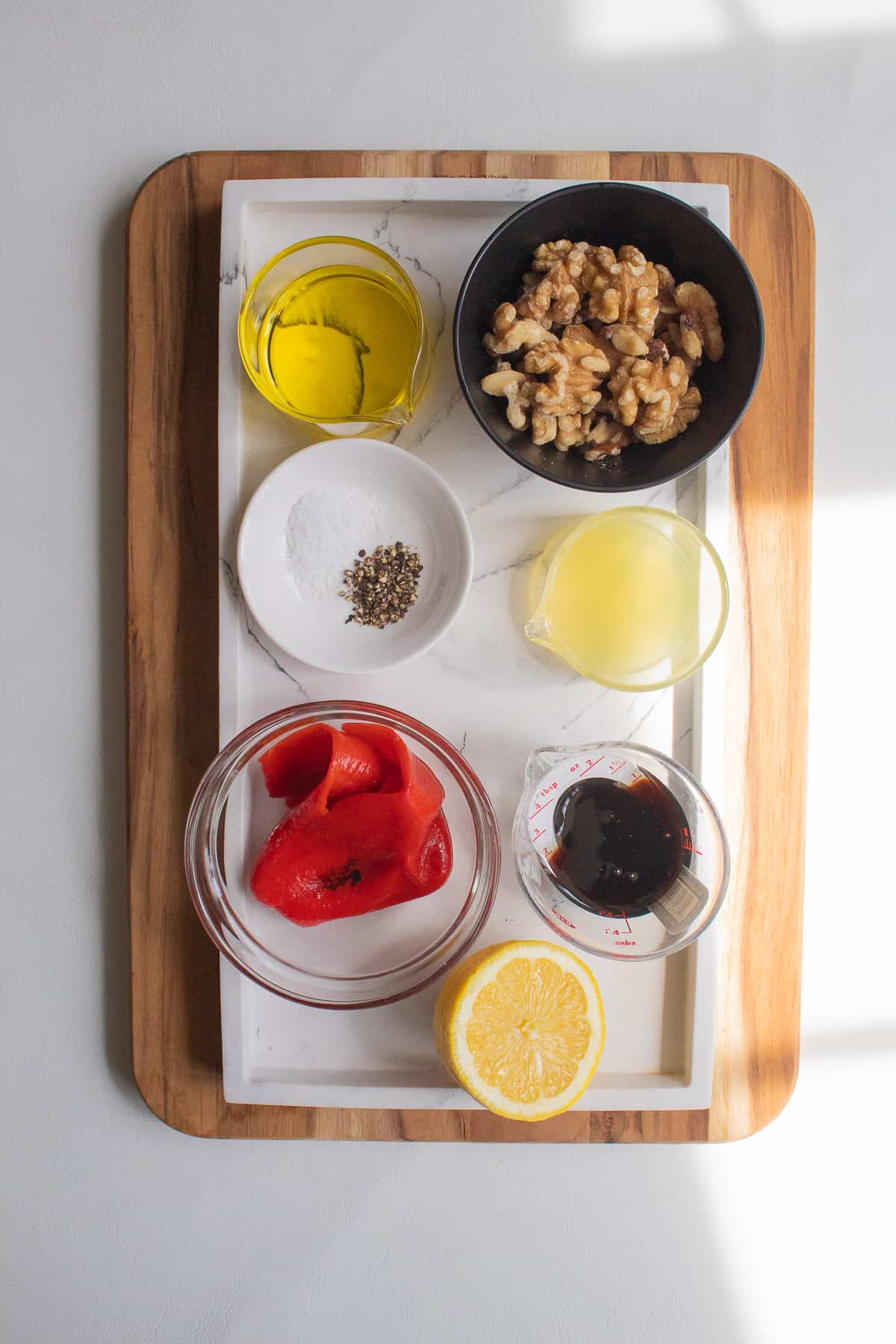 Ingredients for the salad dressing are arranged in small bowls on a white tray.