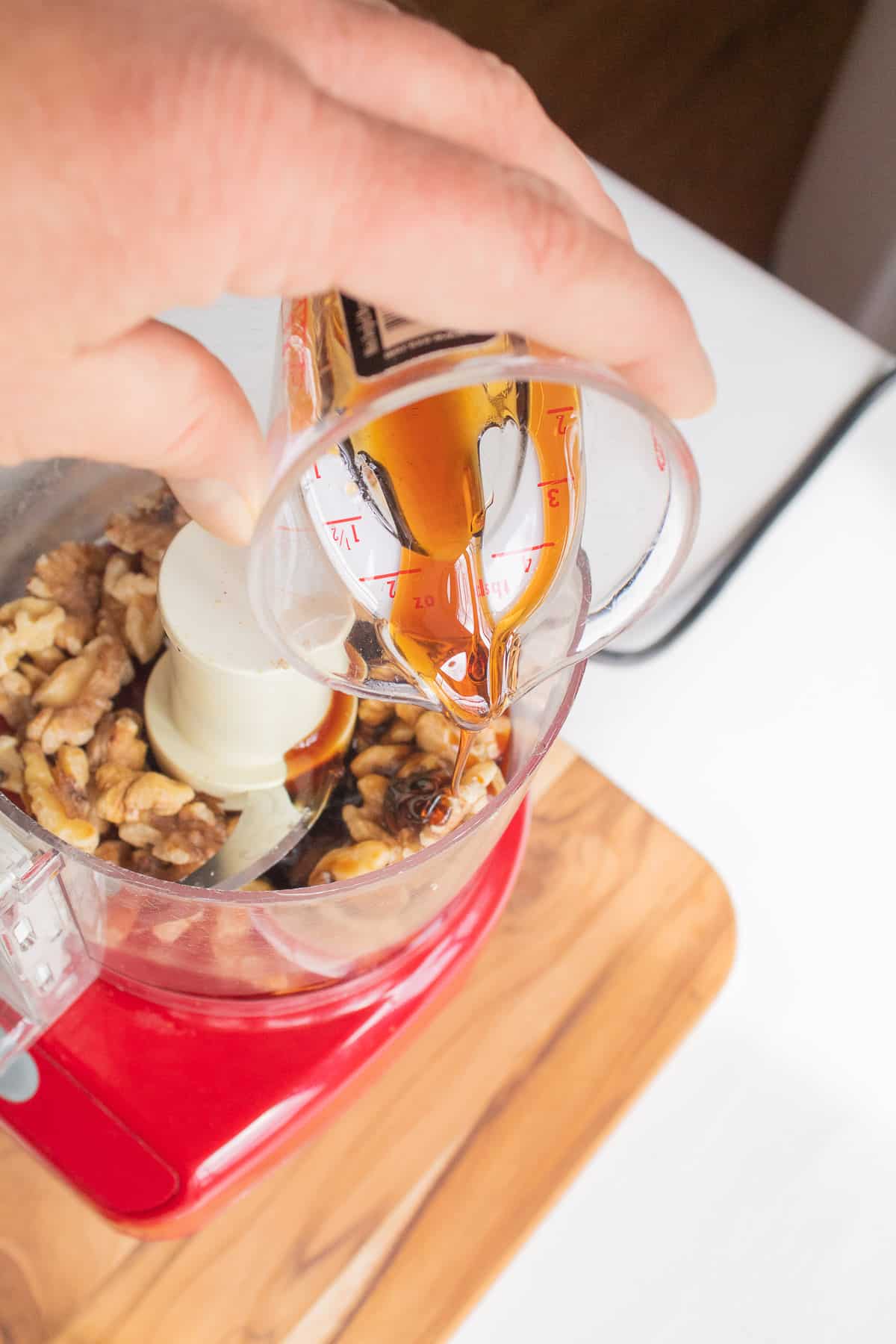 Pomegranate molasses slowly drips from a small measuring cup into the food processor with the remaining dressing ingredients.