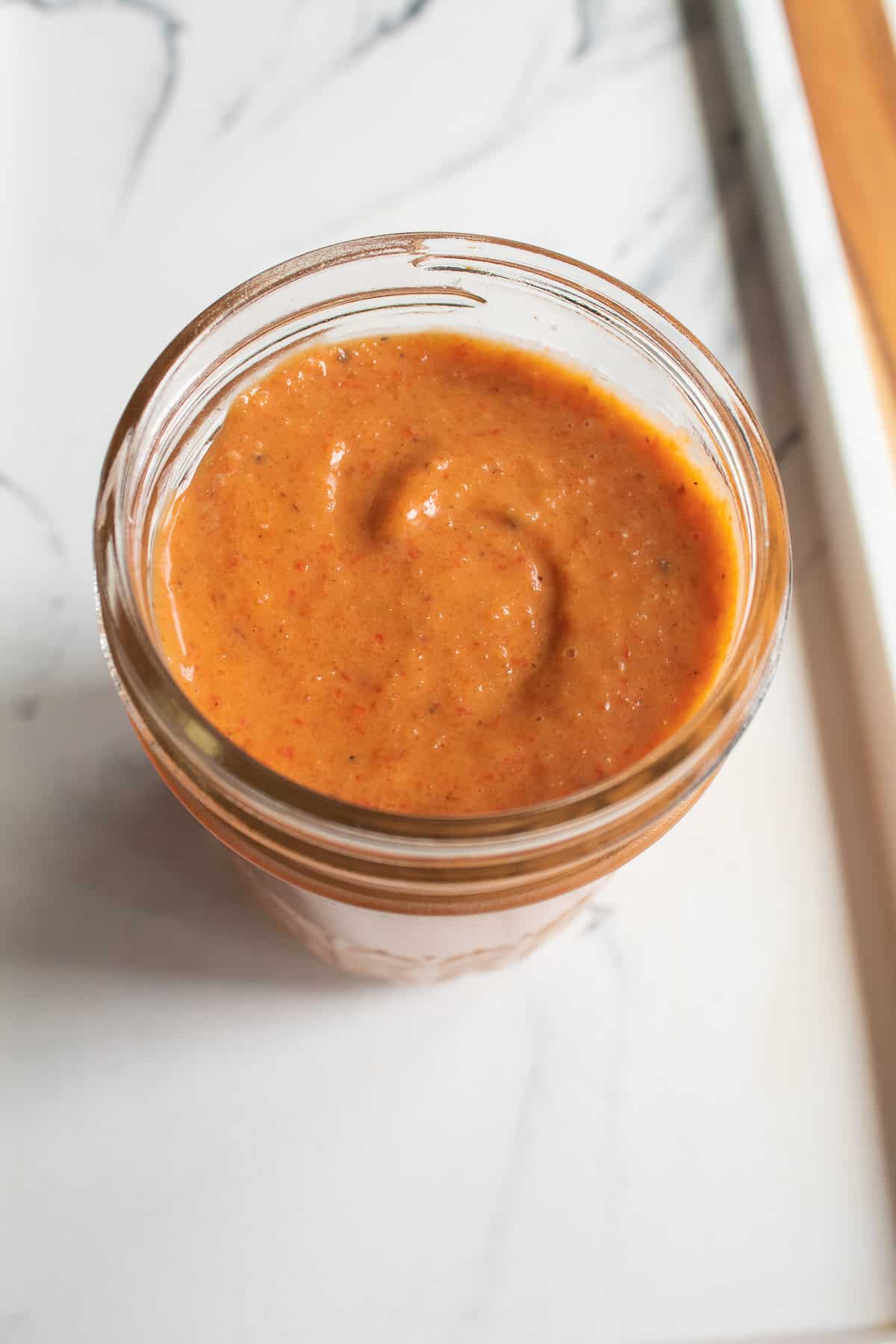 An reddish-orange dressing with specks of black pepper and roasted red pepper is stored in a glass jar.