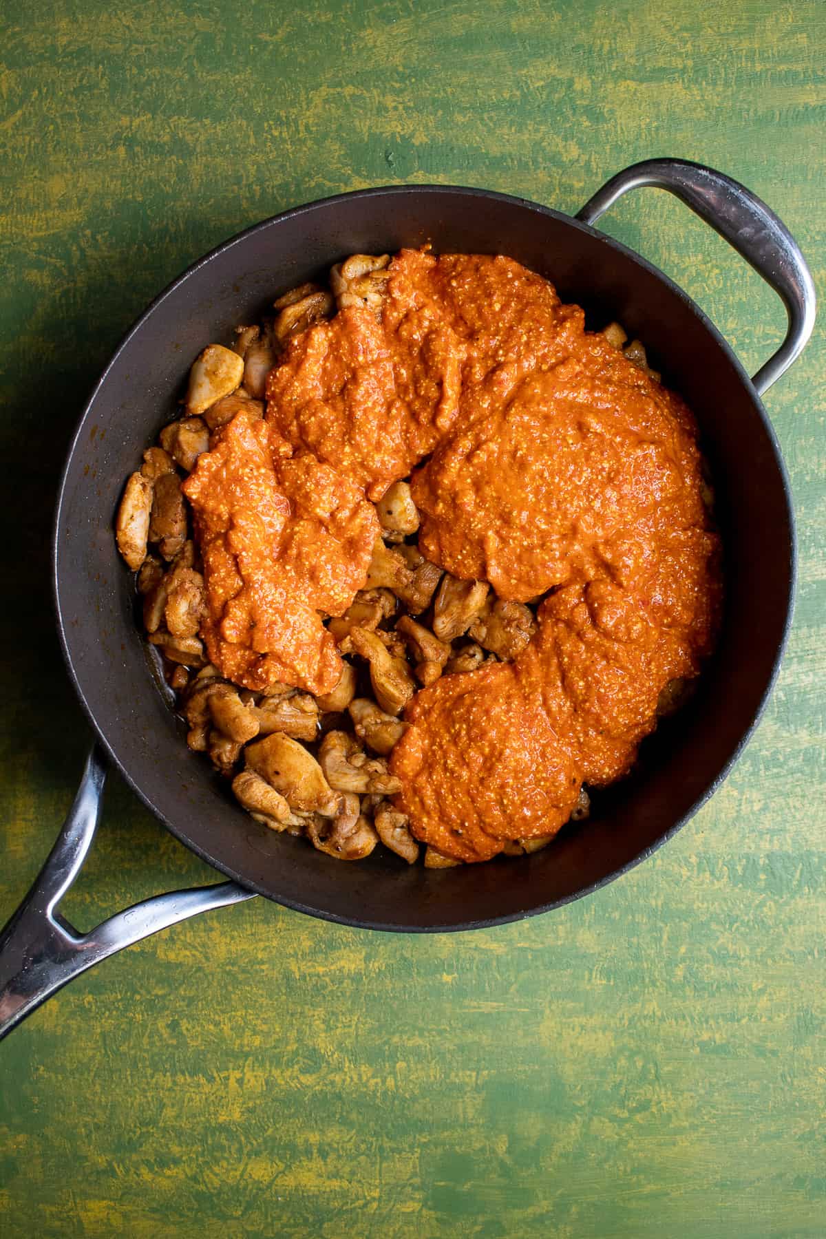 The red pepper sauce poured over the cooked chicken in a black skillet.