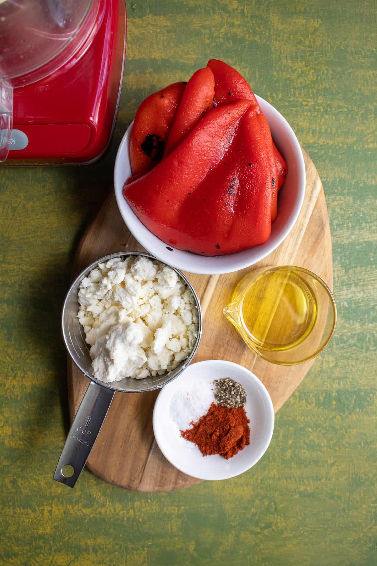 The ingredients for the roasted red pepper sauce (including feta, olive oil, smoked pepper, salt, and pepper) arranged on a small wooden cutting board.