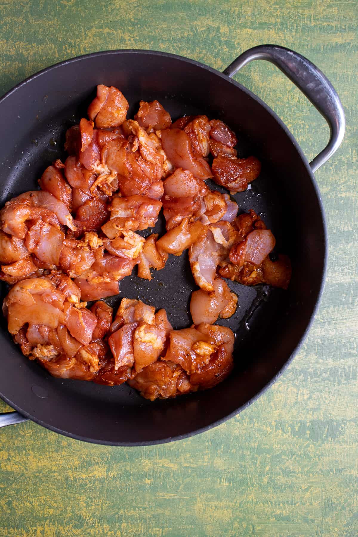Chunks of seasoned chicken thighs in the bottom of a black skillet.
