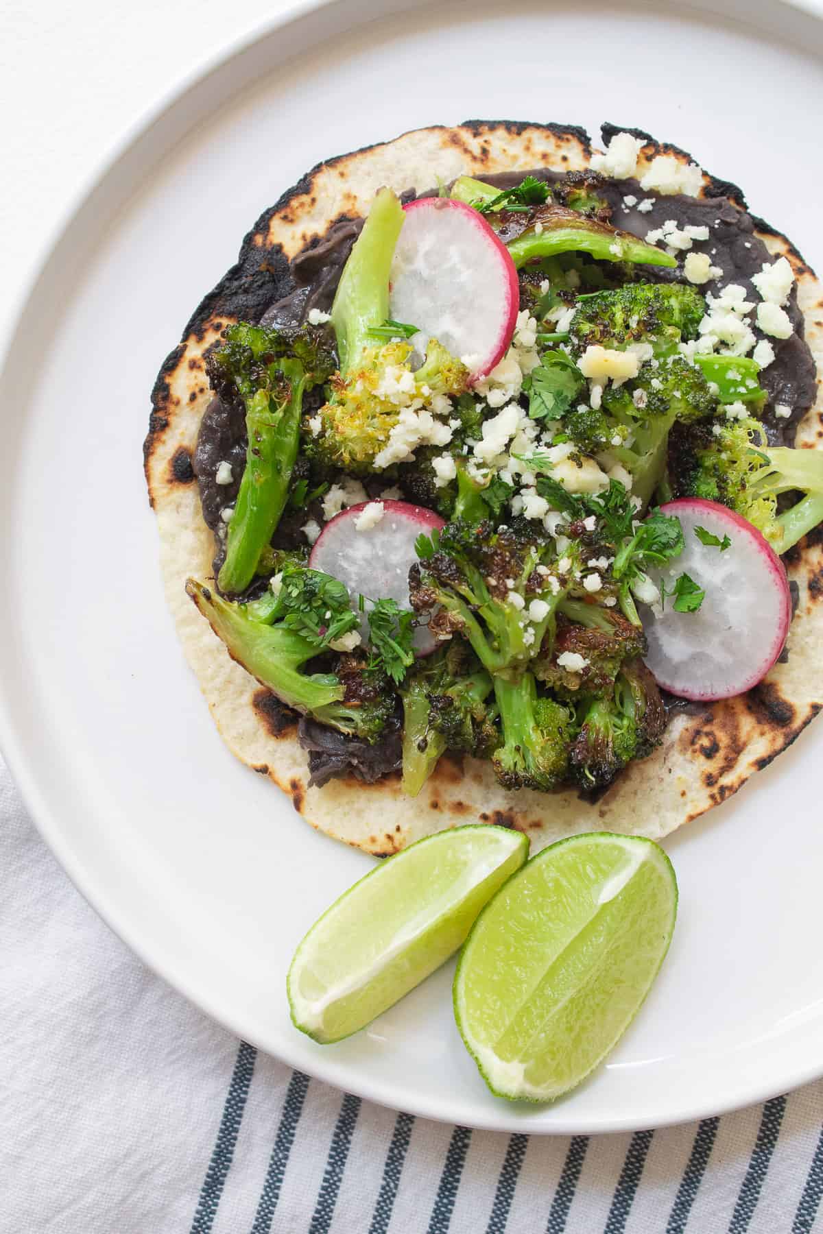 One bean and broccoli taco with a charred tortilla is topped with radishes, cilantro, and crumbled cheese.