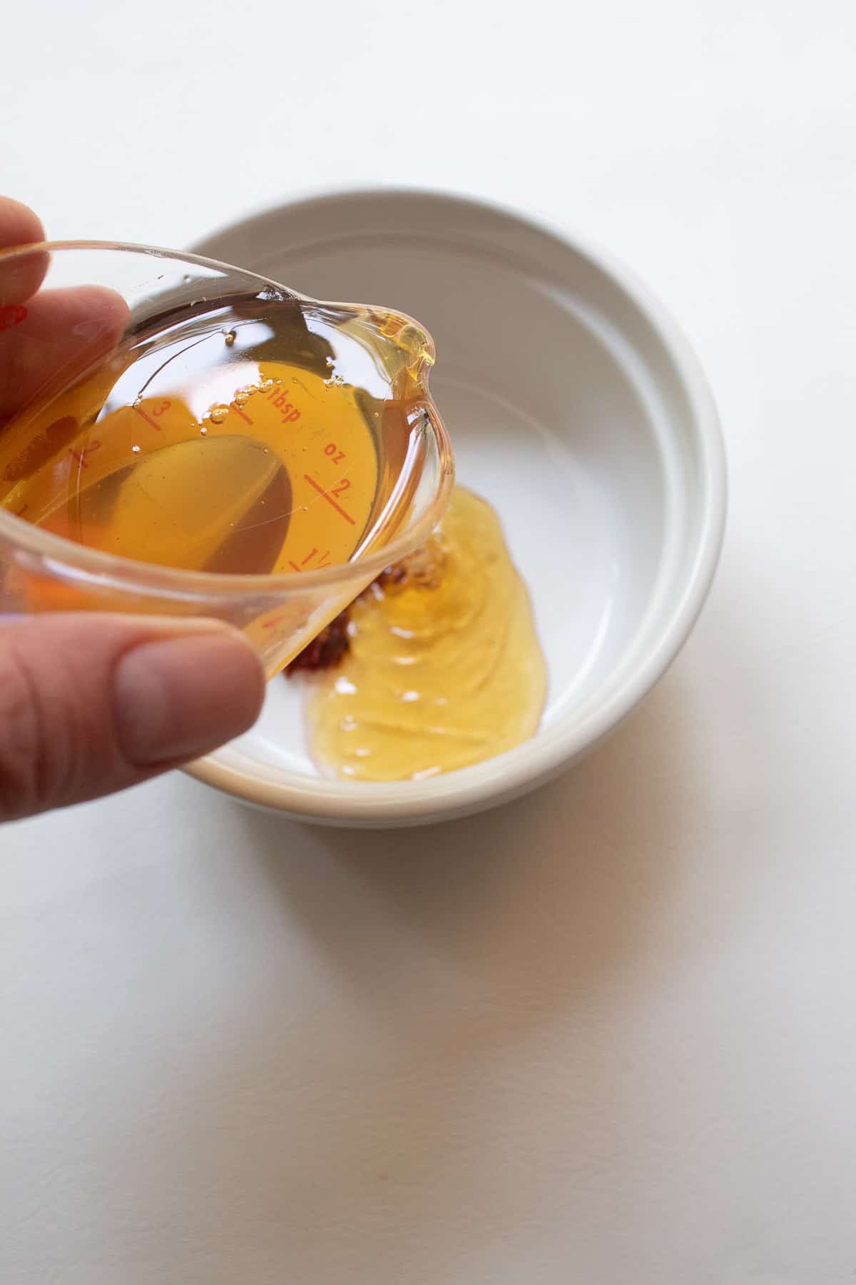 Honey pours from a small measuring cup into a white bowl.