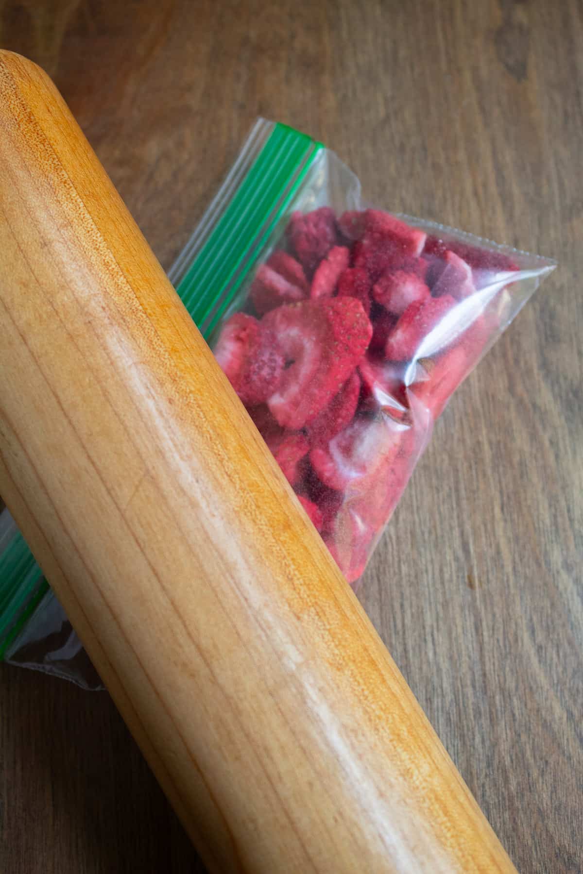 A rolling pin crushing freeze-dried strawberries in a zip bag.